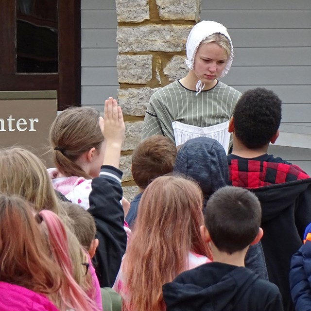 An interpreter in period clothing greets students in front of the visitor center
