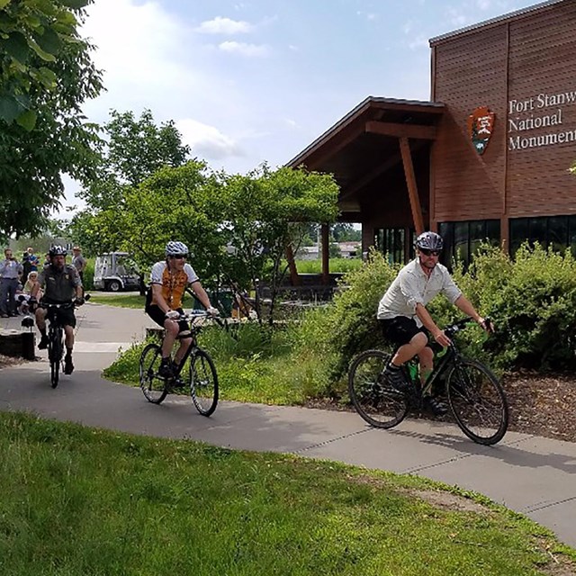 Three people cycle along the fort trail through greenery.