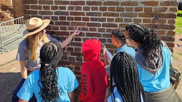 A ranger points at fingerprints captured in bricks while a group of schoolchildren looks on
