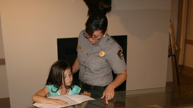 Park Ranger points out items in museum display case to two Jr. Rangers