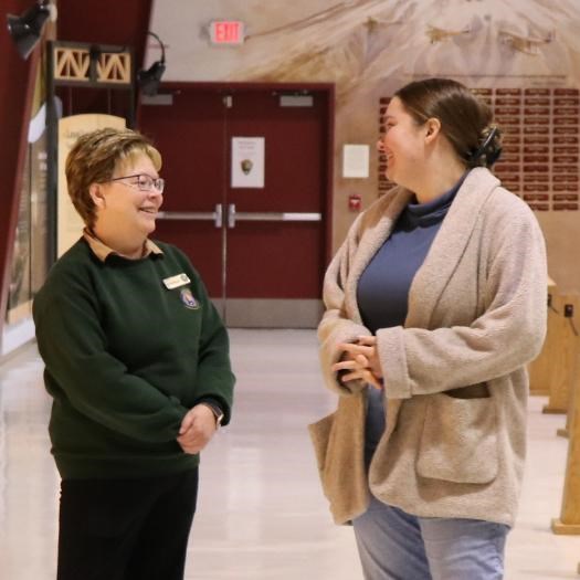 A woman wearing NPS volunteer uniform talks with another woman in an air museum setting