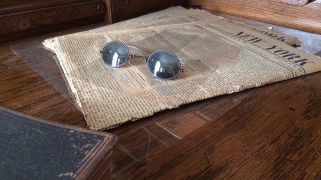 A historical newspaper on a wooden desk with a pair of glasses on top