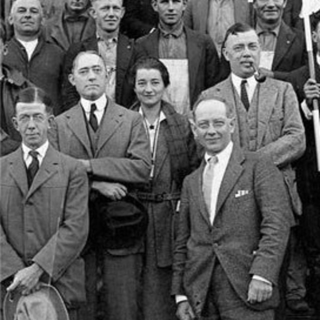 Black and white of many men wearing suits with one woman 