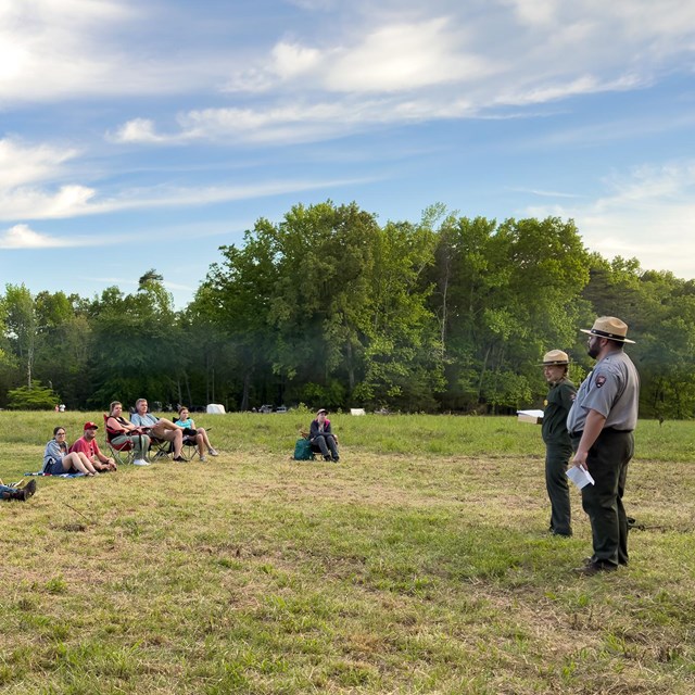 Two park rangers speak to 25 people in a field.