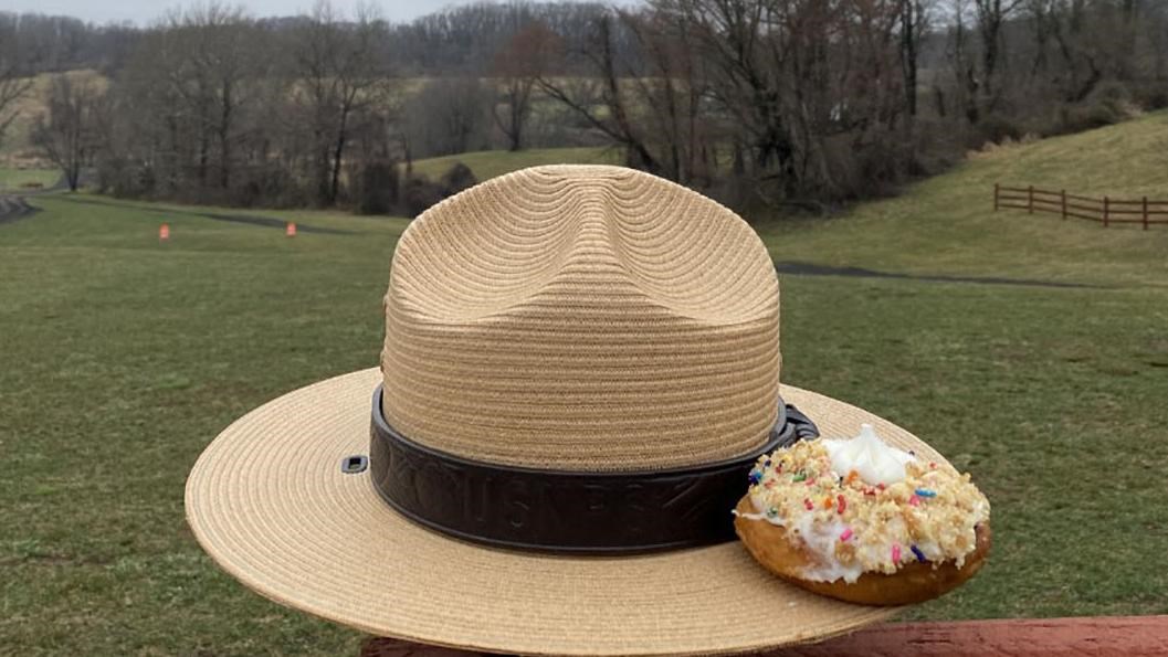 A cupcake with the number 5 sits on the edge of a ranger hat with rolling hills in the background.