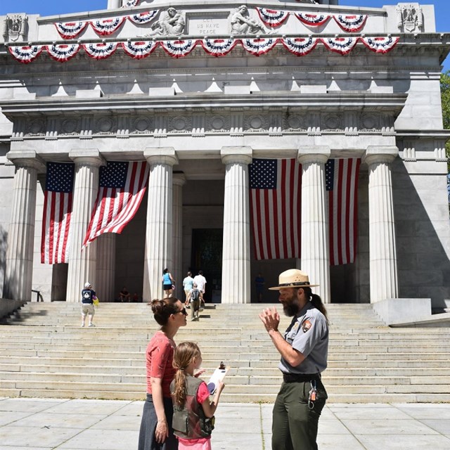 Park Ranger interacts with a Junior ranger in front the columns, steps, and flags at the mausoleum