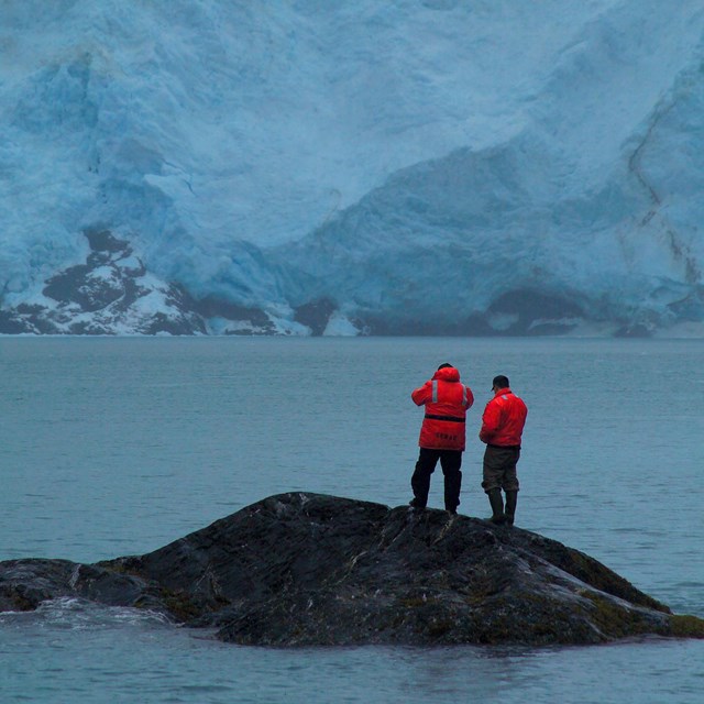 scientists on tiny island with massive tidewater glacier in background