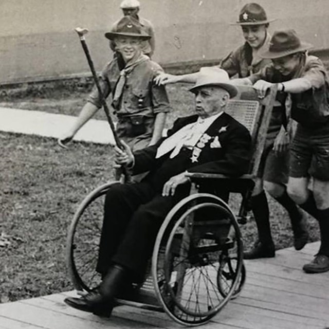 A group of boy scouts help push a veteran of the Battle of Gettysburg around in his wheel chair.