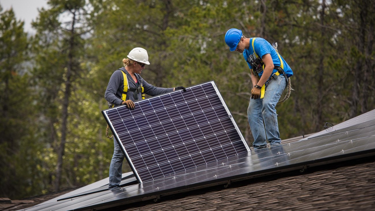 People install a solar panel on a roof.  
