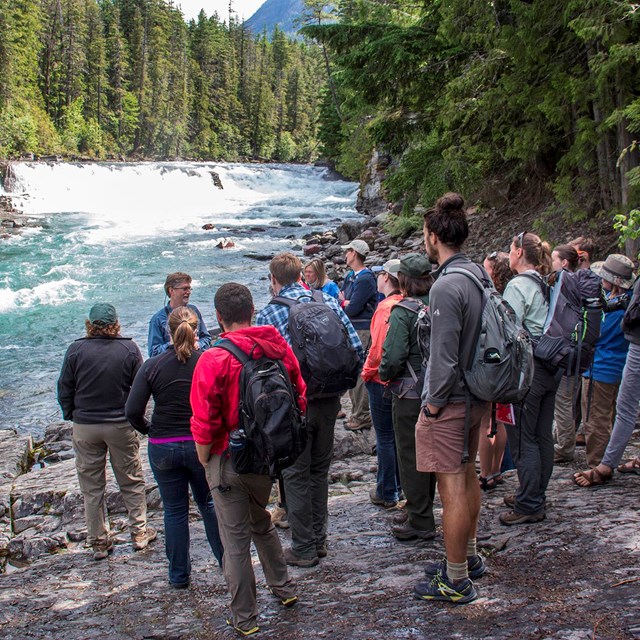 Group of high school students stand by cascading river listening to a teacher