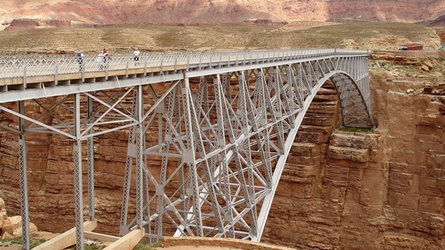 People stand on steel arch bridge anchored in cliff