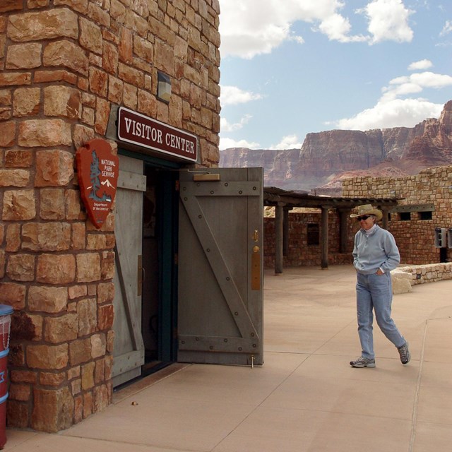 Person walks into open door of stone building under sign reading Visitor Center