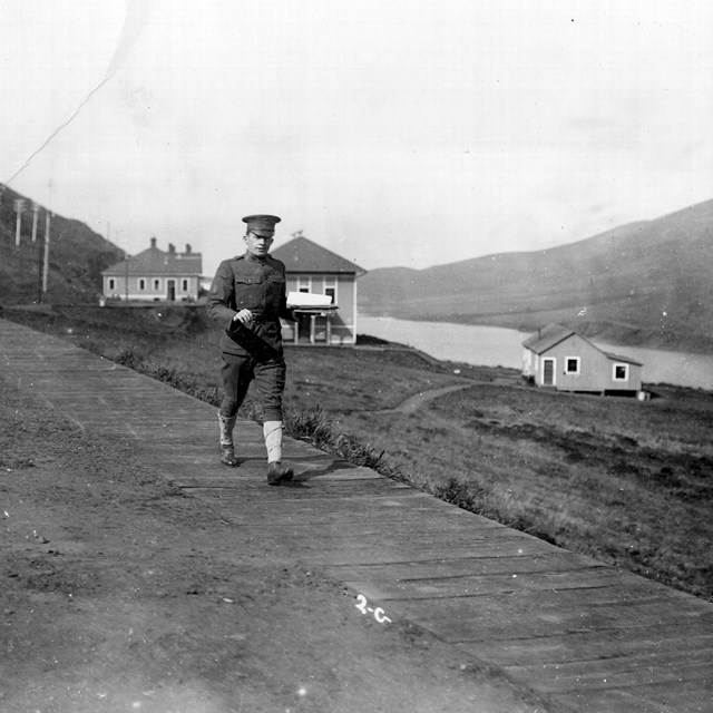 Historic photo of soldier on boardwalk with buildings of Fort Barry and Rodeo Lagoon behind