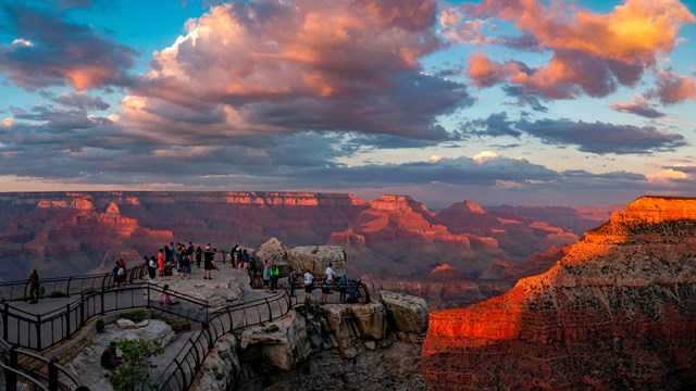 Several dozen sightseers watch the sunset at a scenic overlook at Grand Canyon National Park.