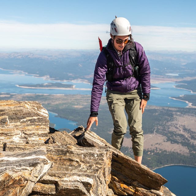 A woman balances on rocks high above a valley.