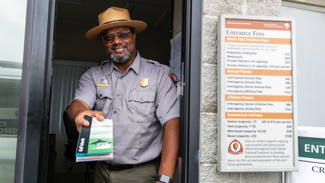 A ranger hands a park brochure to someone sitting in the driver seat of a car.