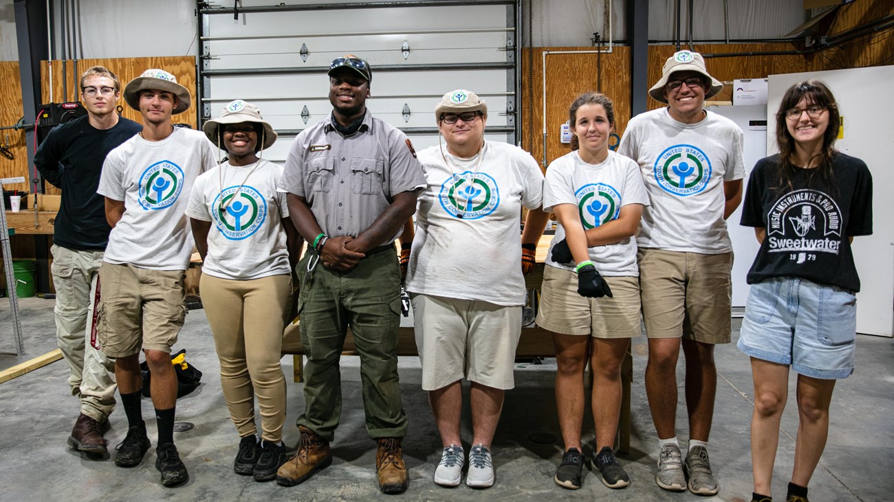 Members of the Youth Conservation Corps and their mentors stand in front of a table they built.