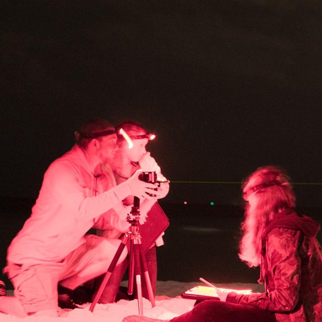 Three people take light measurements of the sky at night.