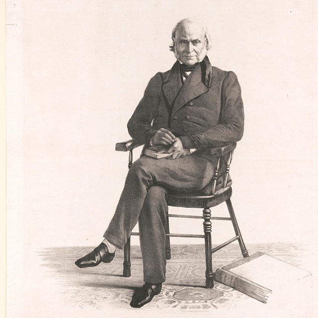 Black and white image of an elderly John Quincy Adams sitting in a wooden chair facing the camera.