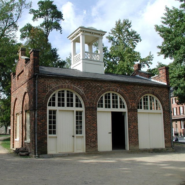Rectangular brick building with three arched entrances and a white central cupola