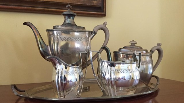 A silver tea set sits upon a tray on a wooden surface.