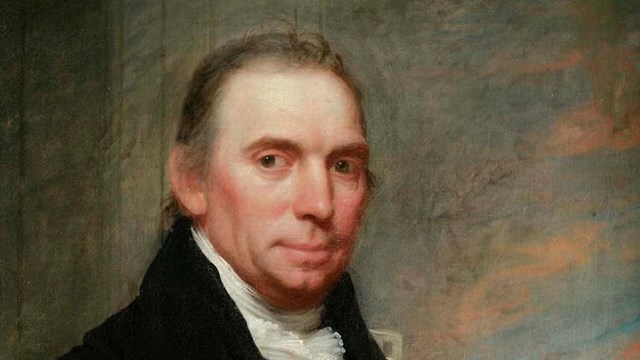 A portrait of John McComb, Jr, who wears a black coat.
