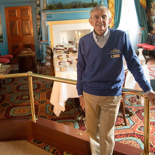 Elderly white male person, named Tom, in the dining room inside of the Hampton mansion.