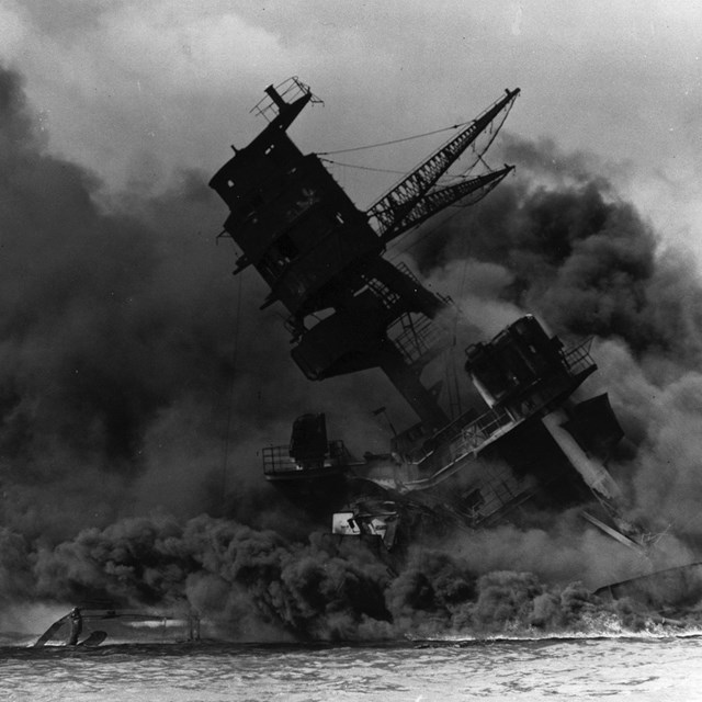 B&W photo of sinking ship surrounded by smoke
