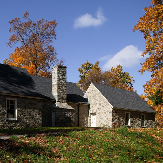 A stone house with steep pitched roof atop a gentle hill.