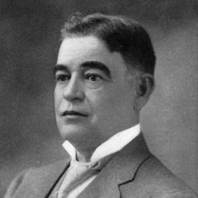 Portrait from late 1800s, a young man in a suit with very defined eyebrows looks off to the side.