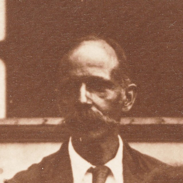 Man with mustache is outside wearing a suit and tie
