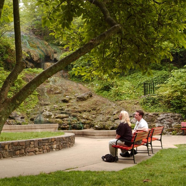 A couple sits on a park bench looking at the hot water cascade in the park.
