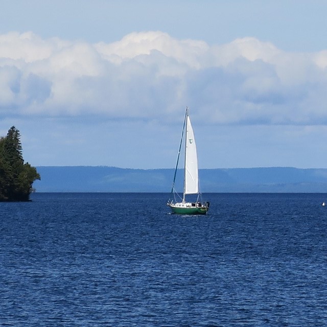 A sailboat in calm waters, sailing towards a smaller island.
