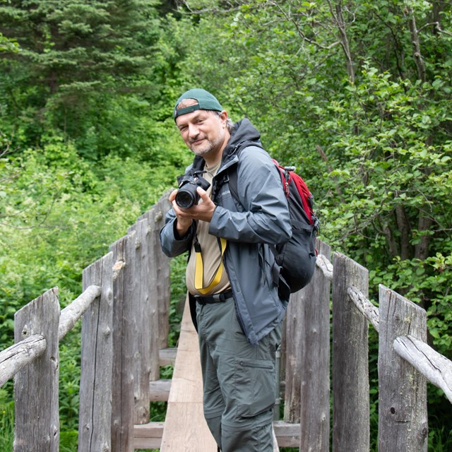 A man standing on a wooden bridge holding a camera.