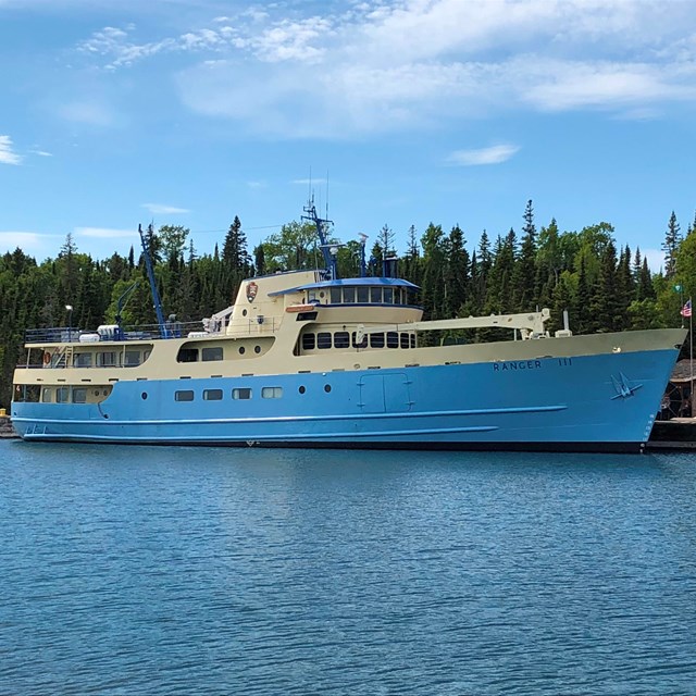 A large blue boat is shown at a dock with blue skies in the background.