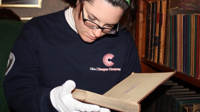 Visitor handling a book from the Garfield Home with white gloves.