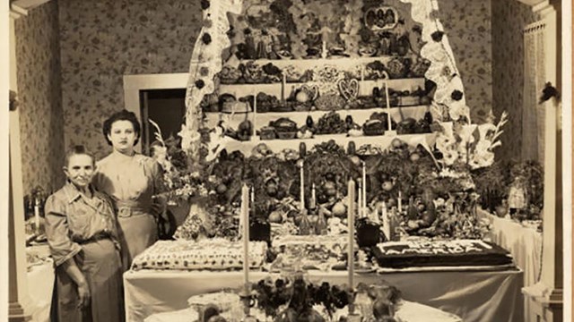1940: an adult daughter and elderly mother stand next to a large multi-tiered altar