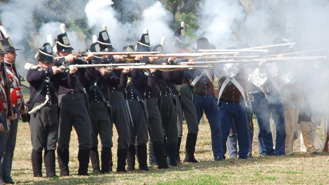 Soldiers fire muskets, causing the air to fill with smoke.