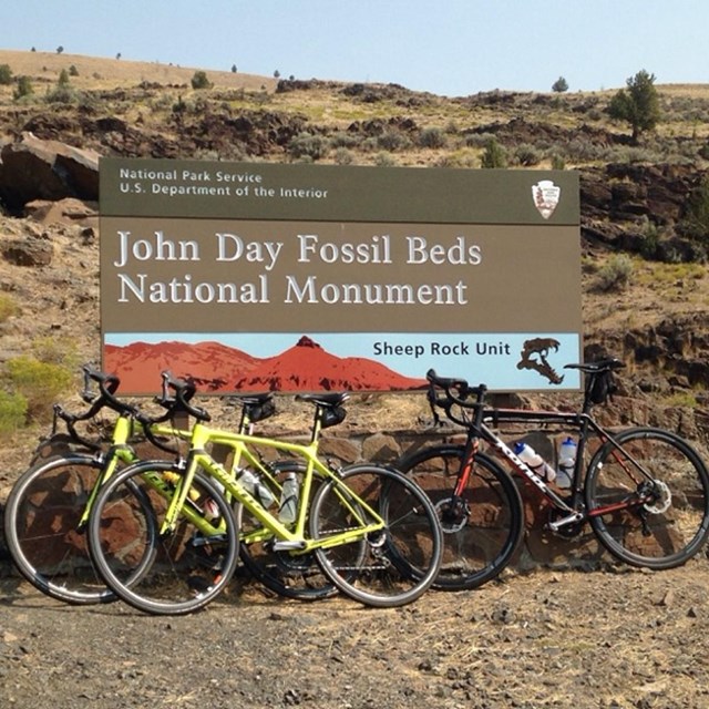 Three bicycles leaning against a John Day Fossil Beds National Monument entrance sign