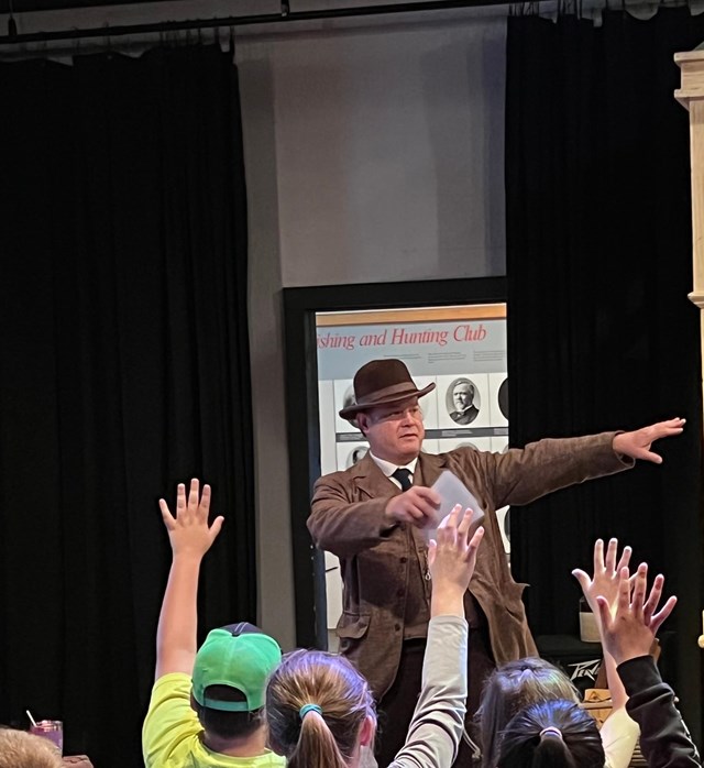 A park ranger in period clothes gives a program to a group of school students.