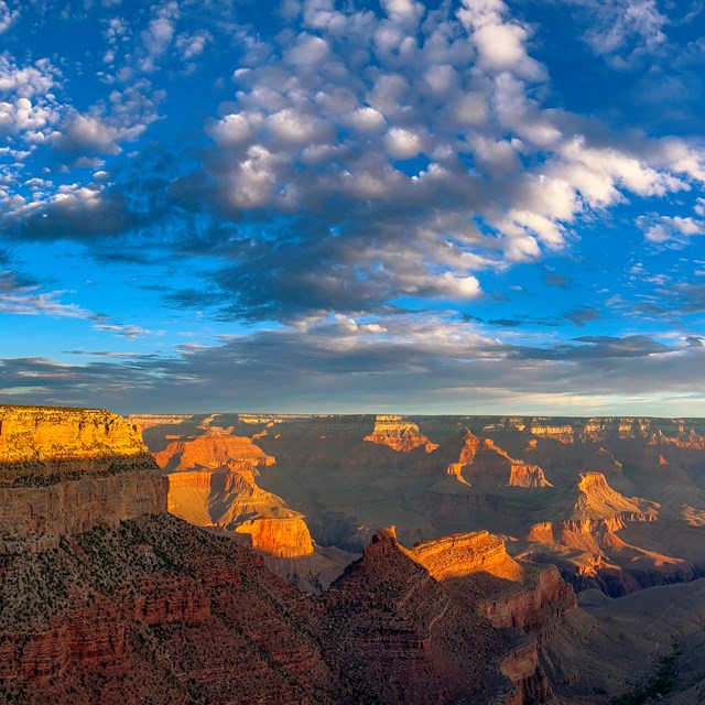 a checkerboard of patchy clouds fills the sky above a vast canyon landscape of colorful peaks
