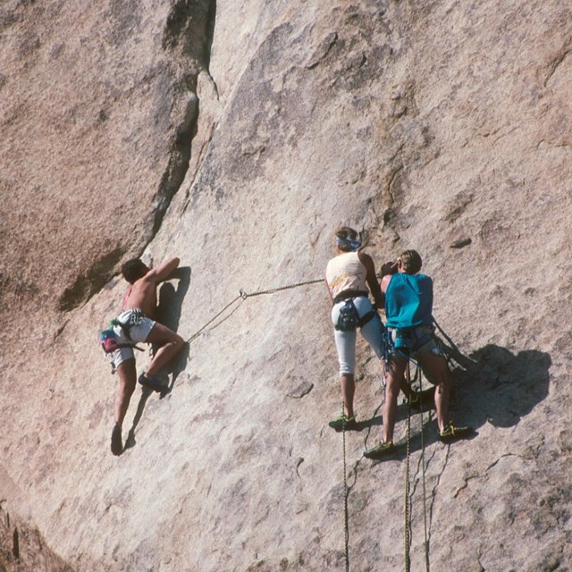 Three people rock climbing on a cliff face