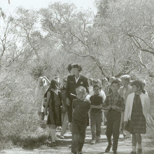 A black and white photo of a female ranger leading a group of kids