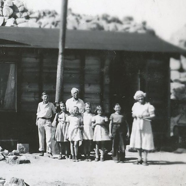 a black and white photograph of school children and adults in front of an old school house