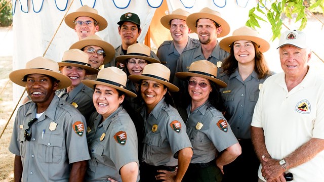 A group of NPS employees and volunteers pose in front of a tent for a photo