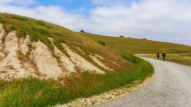 A wide trail winds around a grassy hill