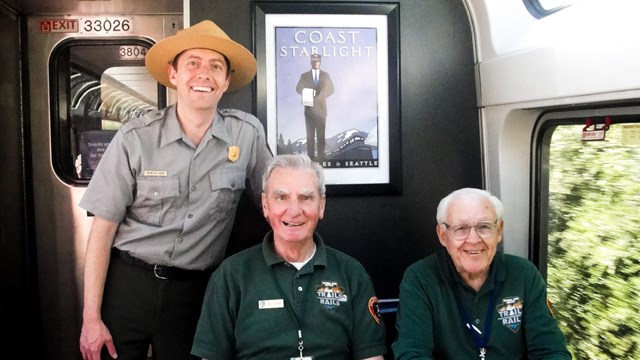 A ranger and two volunteers gather at a table aboard the Coast Starlight train