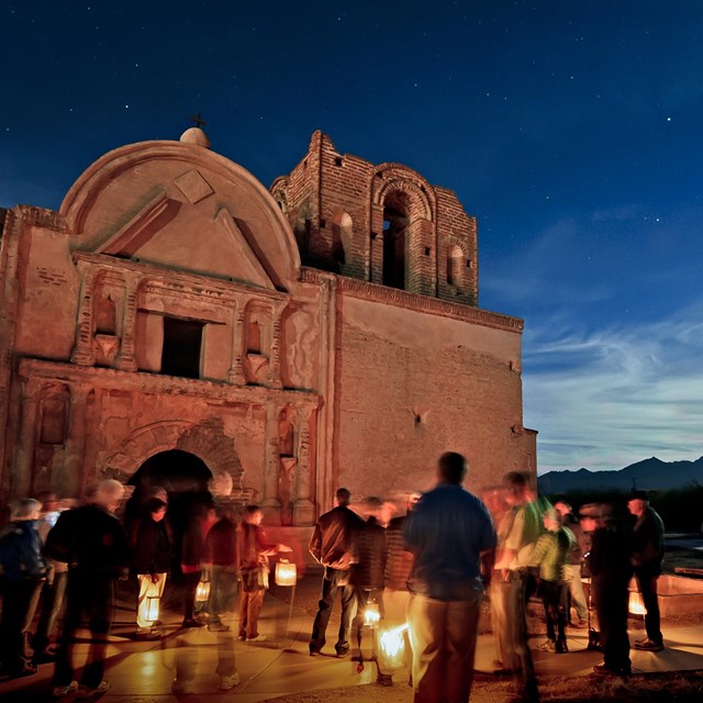 group of visitors with candle lanterns in front of church with full moon in background