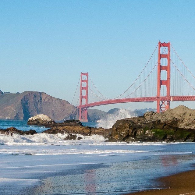 Red Golden Gate Bridge with brown and green headlands and a rocky beach with waves