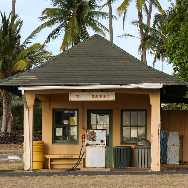 A small tan building with a dark shingled roof. A sign in front reads No Smoking. 